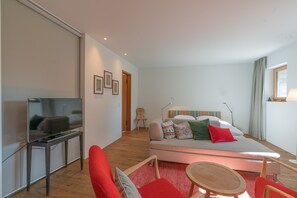 A modern hotel room with a flat-screen TV, a sofa bed, a small table, and a chair. - Chesa Piol Studio – Modern Studio with a View & Wellness Facilities (Maloja)
