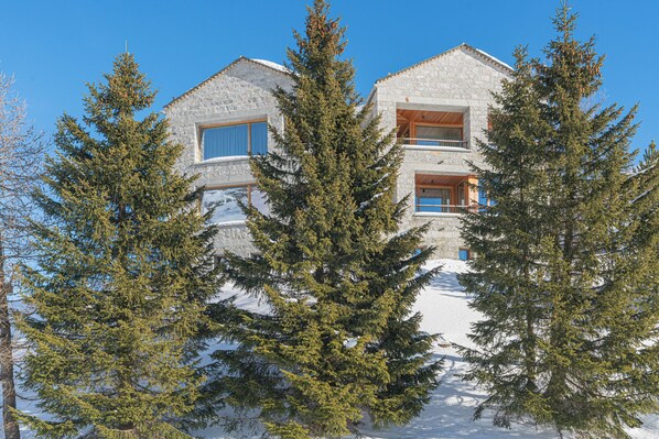 A stone building with multiple windows and balconies, surrounded by snow and evergreen trees. - Chesa Piol Studio – Modern Studio with a View & Wellness Facilities (Maloja)