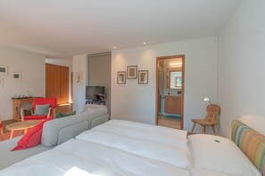 A modern hotel room with a large bed, a sofa, a red chair, a small table, and a TV. - Chesa Piol Studio – Modern Studio with a View & Wellness Facilities (Maloja)