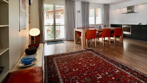 A modern kitchen with a stove, a dining area with a table and chairs, and a large window with curtains. - Residenza Alpenrose 19 – Stylish flat with 2 terraces & panoramic views (Sils/Segl Maria)
