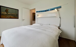 Ein ordentlich bezogenes Bett mit weißer Bettwäsche, ein Bild an der Wand und eine Wandleuchte.
