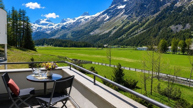 A balcony with a table and chairs, overlooking a mountain landscape with snow-capped peaks and a green valley. - Residenza Alpenrose 19 – Stylish flat with 2 terraces & panoramic views (Sils/Segl Maria)