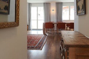 Ein Essbereich mit Holztisch und Stühlen, einem gemusterten Teppich und einem großen Fenster mit Vorhängen.