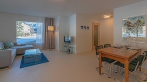 A modern living room with a sofa, coffee table, TV, and dining area with chairs and a table. - Chesa Lagrev 3 – Helle Duplexwohnung mit Garten (Sils/Segl Maria)