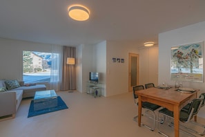 Ein modernes Wohnzimmer mit einer Couch, Couchtisch, Fernseher und einem Essbereich mit Stühlen und Tisch.