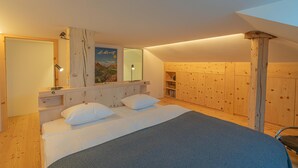 A bedroom with a bed, bedside tables, a mirror, and wooden paneling. - Chesa Lagrev 3 – Helle Duplexwohnung mit Garten (Sils/Segl Maria)