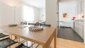 Una cocina moderna con armarios blancos, un comedor con mesa y sillas de madera, y una isla de cocina con una cesta.