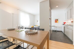 Eine moderne Küche mit weißen Schränken, einem Essbereich mit Holztisch und Stühlen sowie einer Kücheninsel mit Korb.