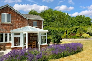 A brick house with a conservatory, surrounded by a garden with purple flowers. - Charming Countryside Cottage with Private Hot Tub (Blandford Forum)