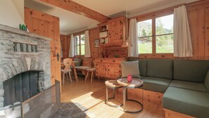 L’intérieur d’un chalet chaleureux, avec une cheminée en pierre, des meubles en bois et de grandes fenêtres.