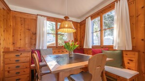 L’intérieur d’un chalet en bois comprend une table à manger, des bancs, un lustre et de grandes fenêtres.