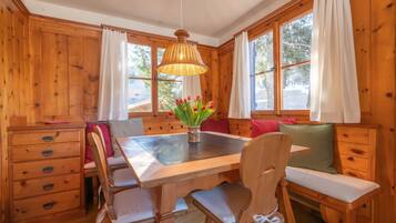L’intérieur d’un chalet en bois comprend une table à manger, des bancs, un lustre et de grandes fenêtres.