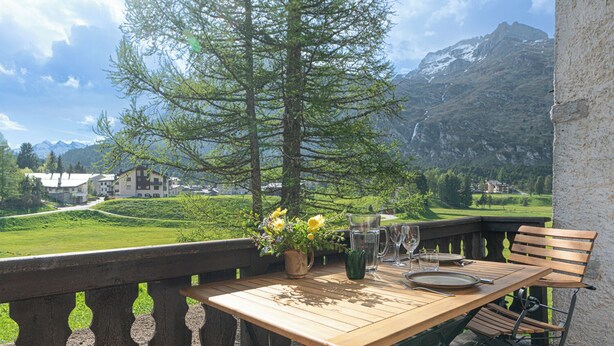 Une table en bois installée à l’extérieur, avec vue sur la montagne, un vase rempli de fleurs et un banc.
