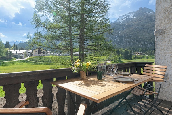 Ein Holztisch draußen mit Blick auf die Berge, eine Vase mit Blumen und eine Bank.