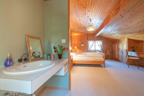 Ein Schlafzimmer mit Holzboden, einem Bett, einem Schreibtisch und einem Badezimmer mit Waschbecken und Spiegel.