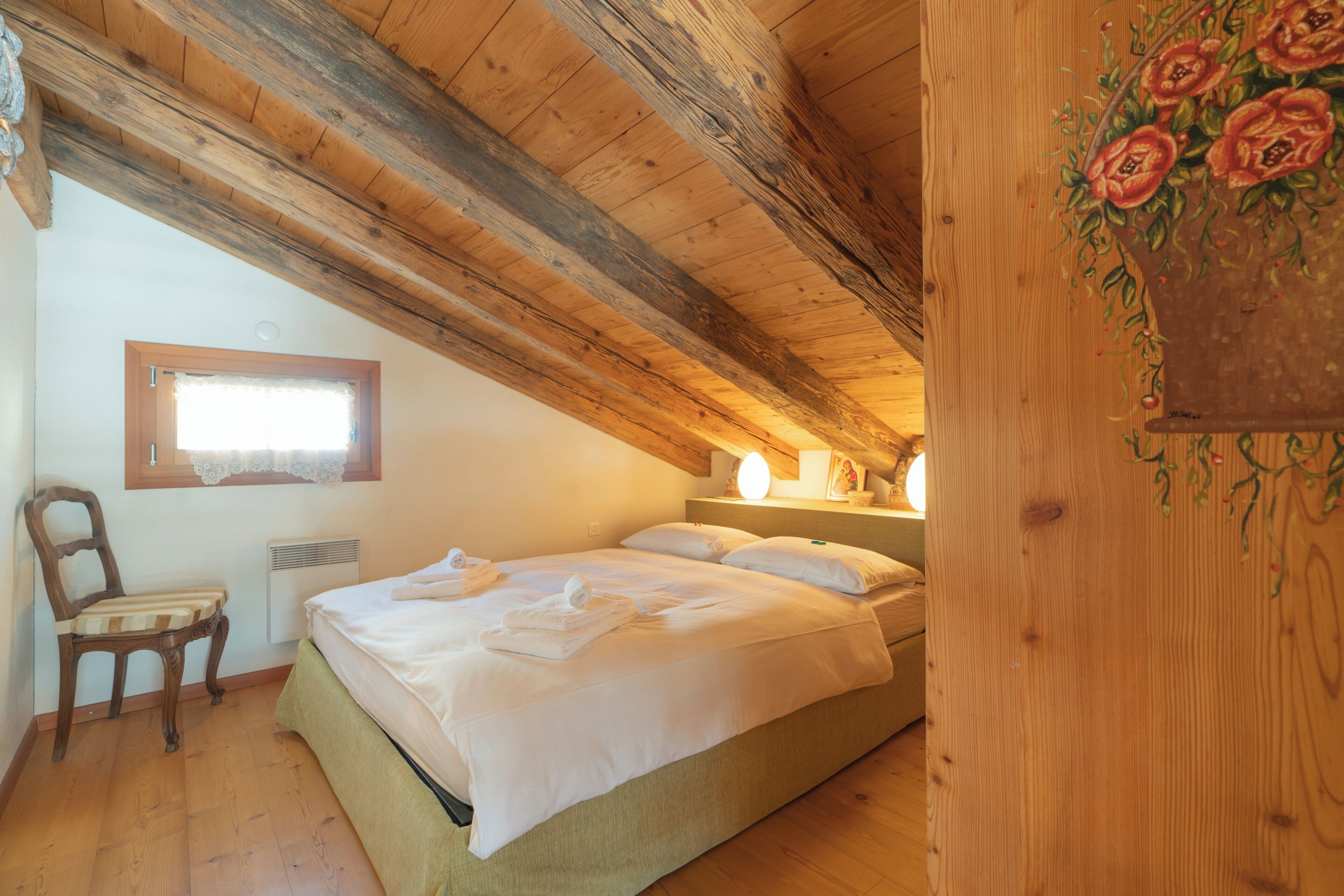 Une chambre avec un plafond en bois, un lit, une chaise et une fenêtre.