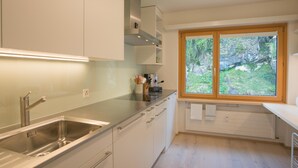 Een moderne keuken met een roestvrijstalen spoelbak, witte kasten, een raam met uitzicht op groen en een inbouwoven.