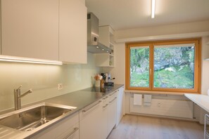 Eine moderne Küche mit Spüle aus Edelstahl, weißen Schränken, einem Fenster mit Blick ins Grüne und einem eingebauten Backofen.