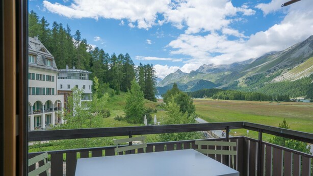 Een balkon met een tafel en stoelen, met uitzicht op een bergachtig landschap met gebouwen en groen.