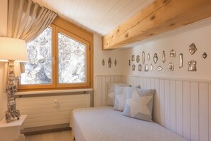 Ein Schlafzimmer mit einem Bett, einem Fenster mit Vorhängen, einer Wand mit Dekoration und einer Holzbalkendecke.