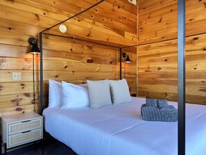 Un dormitorio tipo cabaña de madera con una cama, almohadas, una mesita de noche y dos lámparas fijadas a la pared.