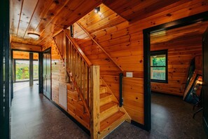 A wooden interior with a staircase, a door leading outside, and a window with a view.