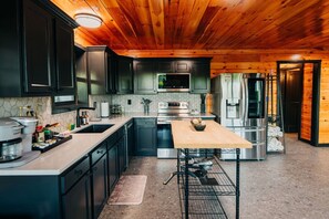 A modern kitchen with dark cabinets, stainless steel appliances, and a wooden ceiling.