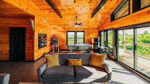 Ein gemütliches Cabin-Interieur mit Billardtisch, einer Couch und einem großen Fenster mit Blick ins Freie.