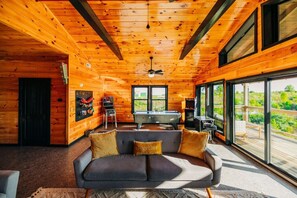 A cozy cabin interior with a pool table, a sofa, and a large window offering a view of the outdoors. - Nerf Blasters | Hot Tub | Mural | Arcade | Sunset (Wolfe County)