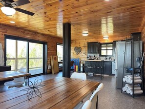 Un interior de madera con una mesa de comedor, sillas, una zona de cocina y un ventanal grande.
