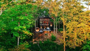 Una cabana envoltada d'arbres, amb terrassa i zona d'estar a l'aire lliure.