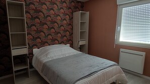 Ein Schlafzimmer mit Bett, Schrank, Heizkörper und einem Fenster mit Jalousien.