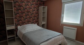 Ein Schlafzimmer mit Bett, Schrank, Heizkörper und einem Fenster mit Jalousien.