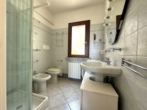 A bathroom with a glass shower enclosure, a bidet, a toilet, and a sink with a mirror above it. - Vacation House Bellavista - Budoni - Muriscuvò (budoni)