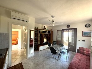 Een woonkamer met een eettafel, stoelen, een bank, een plafondventilator en een boekenkast.