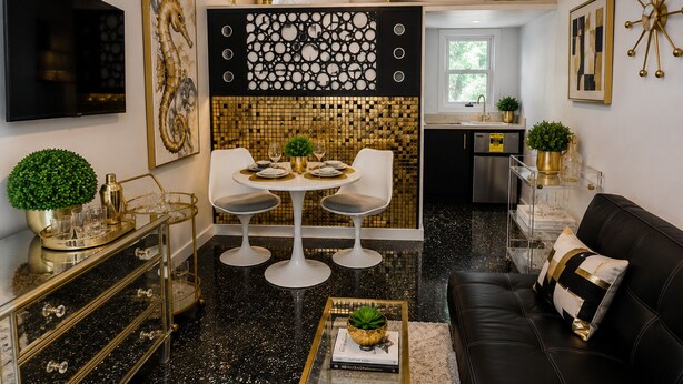 A compact living space with a dining area, kitchen, and seating area, featuring modern decor and a black and gold color scheme. - THE ATOMIC ART MALUTKI DOMER™  HGTV Artist-Designed Tiny House Retreat Sleeps 4 (Fort Myers)