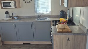 Una cocina moderna con armarios grises, microondas, hervidor y tabla de madera con frutas.