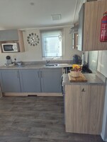 Una cocina moderna con armarios grises, microondas, hervidor y tabla de madera con frutas.