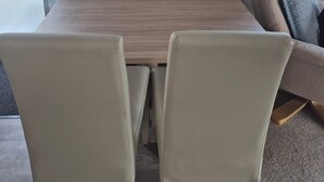 Una habitación con una mesa de madera, cuatro sillas, una obra de arte enmarcada de una mariquita y una ventana con cortinas.