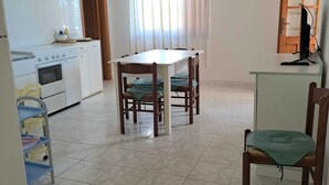 Eine Küche mit Herd, Backofen und Spüle, einem Esstisch mit Stühlen und einem Fenster mit Vorhängen.