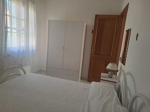 Ein Schlafzimmer mit Bett, Schrank, Holztür, Lampe und Spiegel.