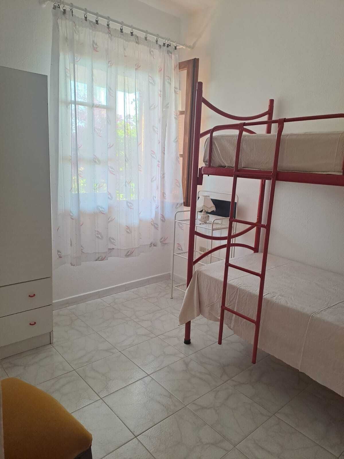 Une chambre de dortoir avec un lit superposé, une armoire et une fenêtre avec des rideaux.