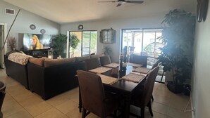 A living room with a sofa, TV, dining table, chairs, ceiling fan, and potted plants. - Tropical Oasis, 3 Bedroom house with pool. (Palm Bay)