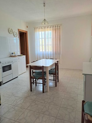 A kitchen with a dining table, chairs, and a window with curtains. - Casa Giovanna - Villa (La Caletta)