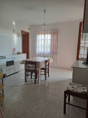 A kitchen with a stove, oven, and dining table with chairs. - Casa Giovanna - Villa (La Caletta)