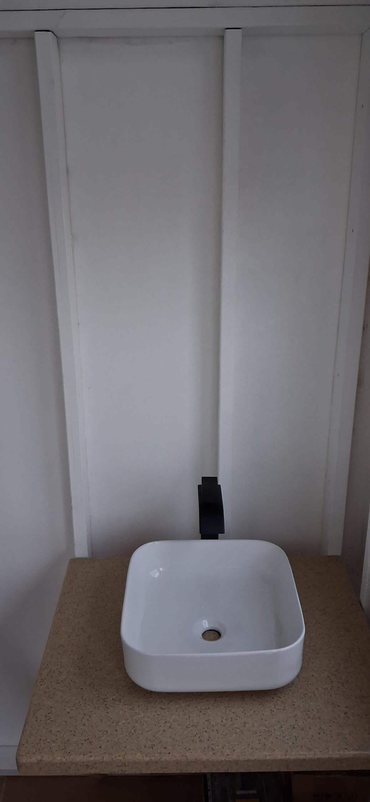 A white rectangular sink with a black faucet on a beige countertop.