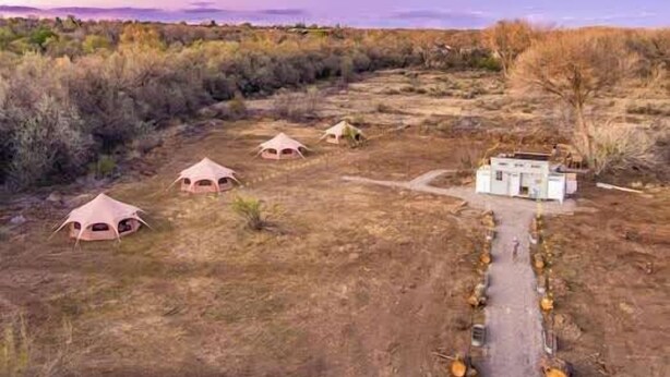 A campsite with several dome-shaped tents and a central building, surrounded by dry vegetation. - Journey South West Tent 3 (Farmington)