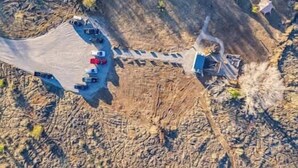 An aerial view of a parking lot with a few vehicles, a building with a sloped roof, and a dirt path leading to the building. - Journey South West Tent 3 (Farmington)