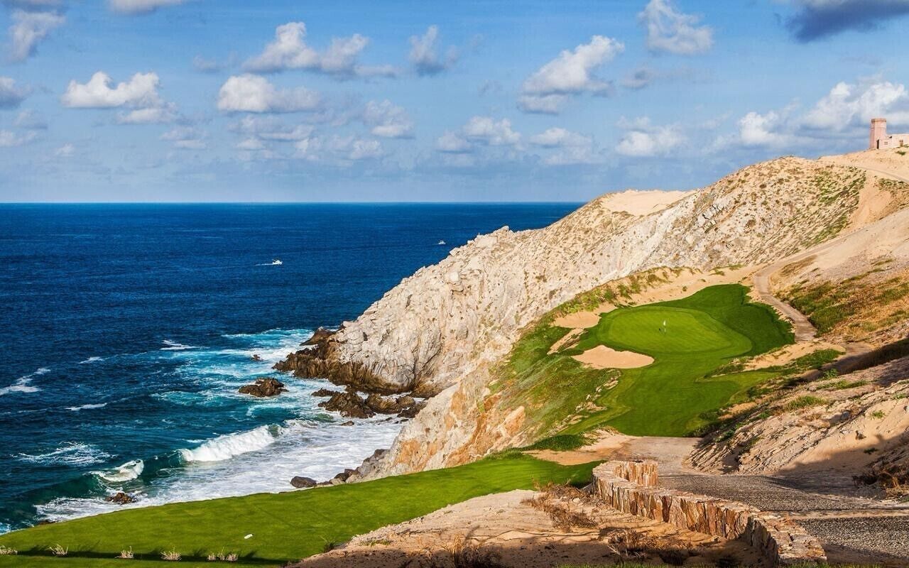 Un paisaje costero con un campo de golf, terreno rocoso y un edificio distante.