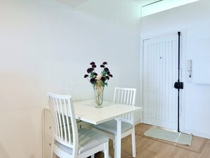 Ett vitt matbord med två stolar, en vas med blommor och en vit dörr med ett svart handtag.